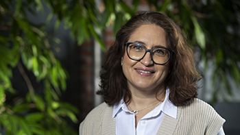 Sonya Trad, kvinna med mörkt lockigt hår, glasögon, ljusa kläder, ler mot kameran.